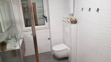 A small bathroom with white tiles, a toilet, a sink, and a shower area.