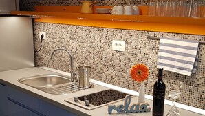 A modern kitchen with a tiled backsplash, a built-in sink, and a countertop with a 'relax' sign. - Galeria Nura (Mostar)