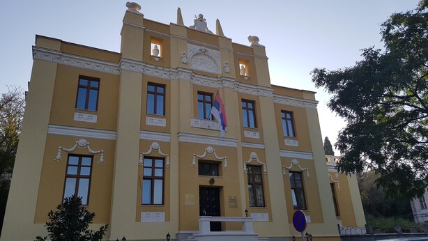 A yellow building with ornate architectural details, including a balcony with a flag, and a no-parking sign. - Galeria Nura (Mostar)