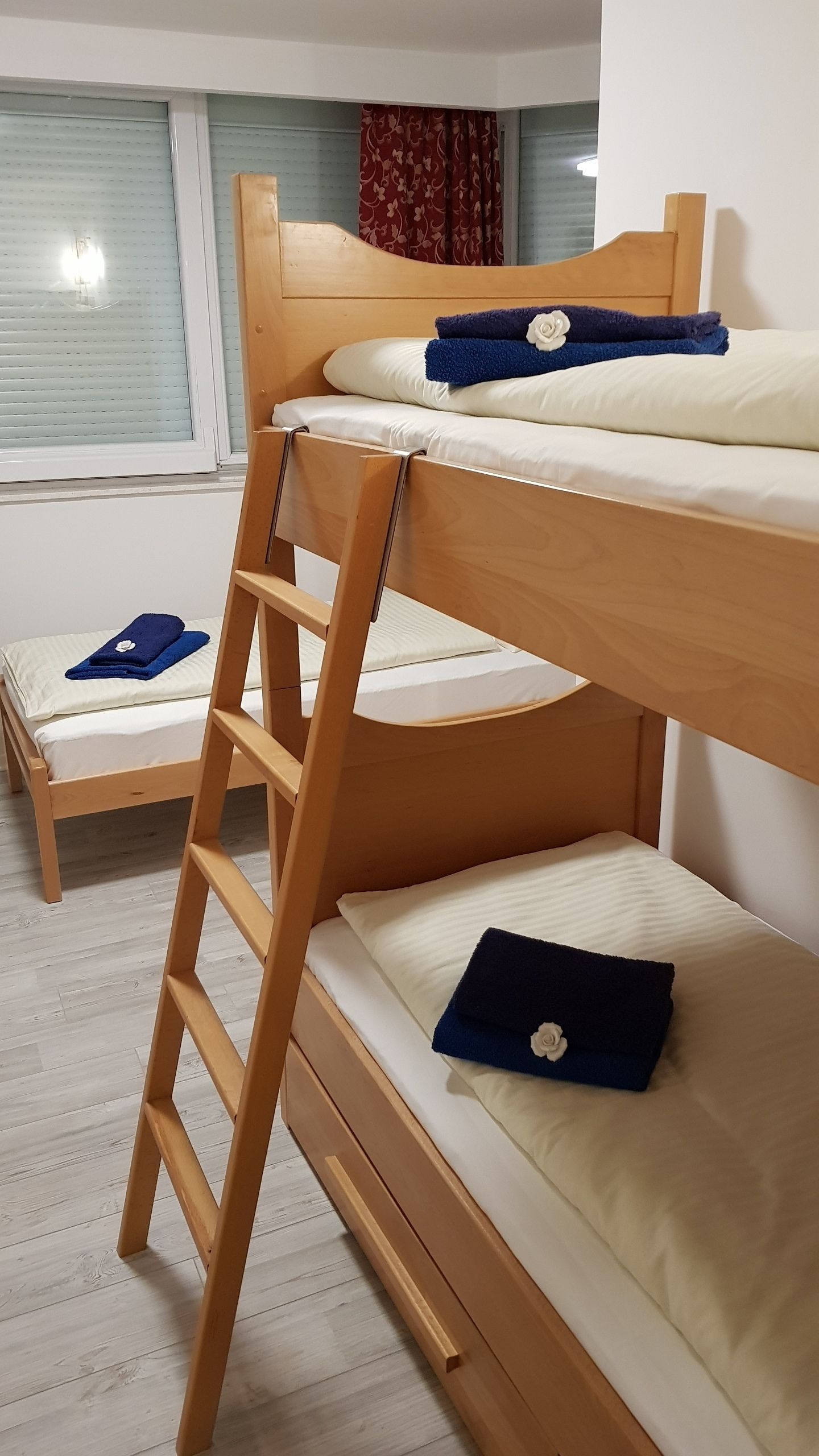 Una cama individual superpuesta con escalera de madera, ropa de cama blanca y una toalla azul con un estampado floral.