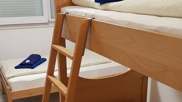 Una cama individual superpuesta con escalera de madera, ropa de cama blanca y una toalla azul con un estampado floral.
