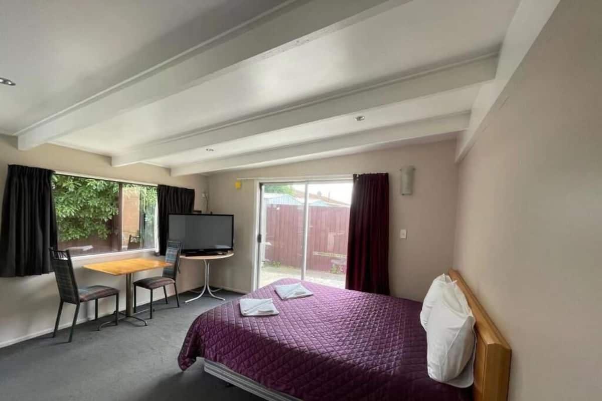 Une chambre d’hôtel comprenant un lit, un bureau avec une chaise, un téléviseur et une porte-fenêtre coulissante donnant sur l’extérieur.