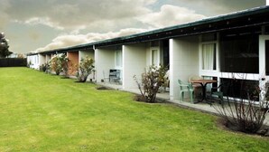 Een rij motelgebouwen met één verdieping, elk met een eigen kamer, een gazon en kleine struiken.