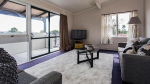 Een woonkamer met een bank, een salontafel, een televisie en een grote glazen schuifdeur die uitkomt op een balkon.