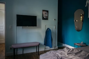 A bedroom with a bed, a bench, a TV, a coat rack, and a small table with a cup.