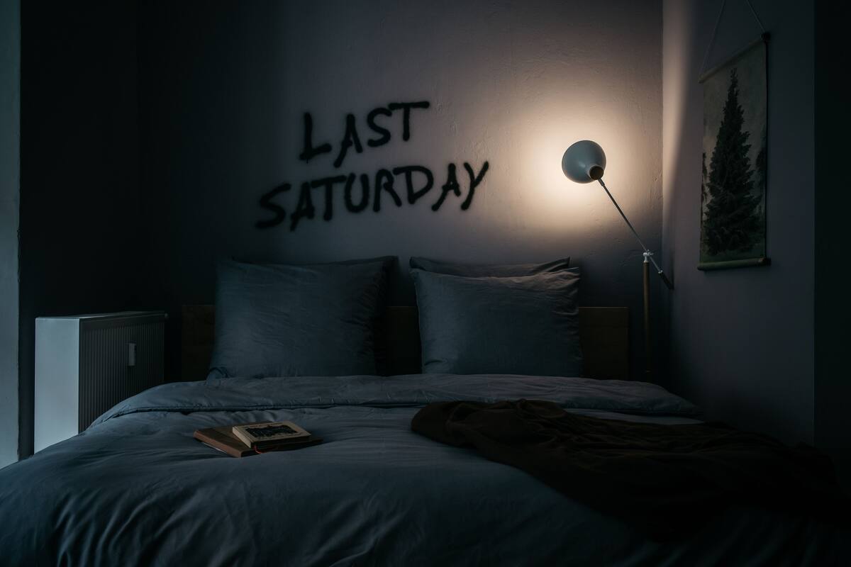 A bedroom with a bed, a wall-mounted lamp, and a painting.
