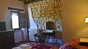 A bedroom with a stone wall, a wooden dresser, a bed with red bedding, and a chair.