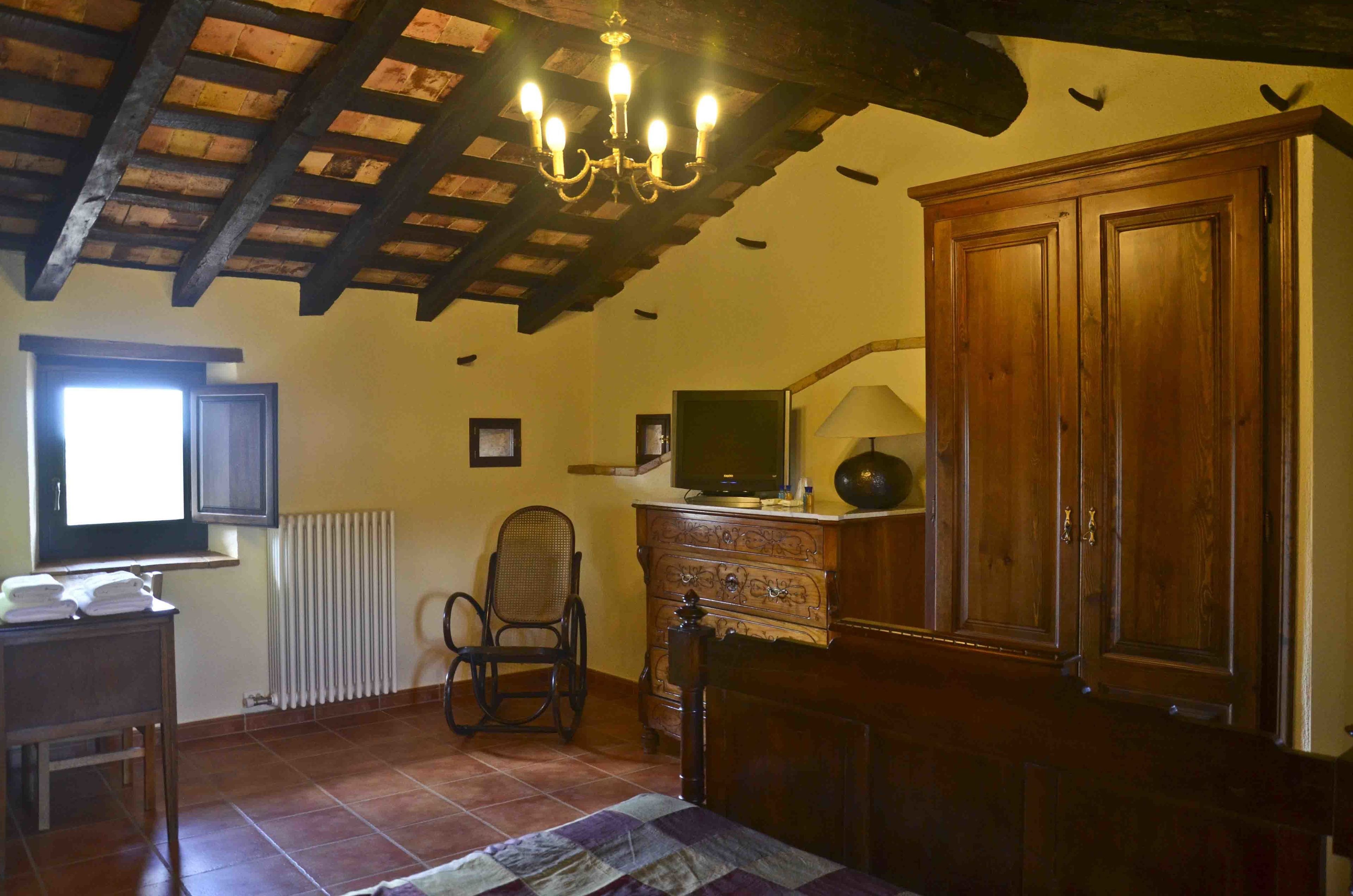 Una habitación con techo de madera, un candelabro, un televisor sobre un mueble de madera, una silla y una cama con colcha.