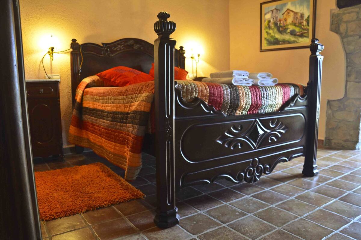 Un dormitorio con cama, mesita de noche, lámpara y un cuadro en la pared.