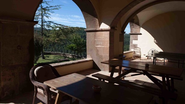 Un patio al aire libre con arcos de piedra, mesas de madera y sillas de mimbre.