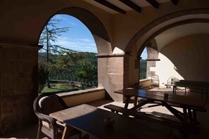 Une terrasse extérieure agrémentée d’arches en pierre, de tables en bois et de chaises en osier.