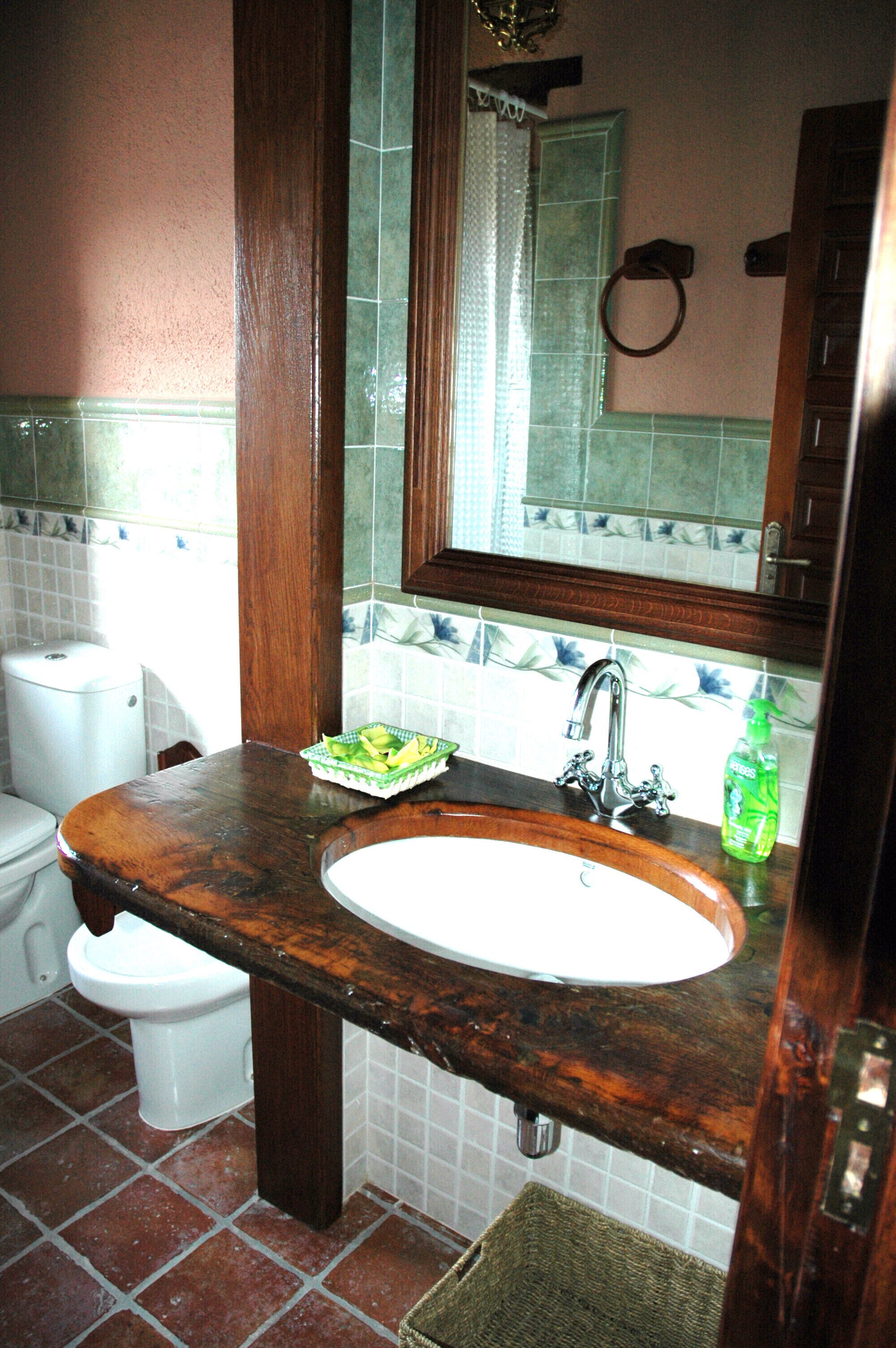 Un baño con tocador de madera, lavamanos blanco, espejo y retrete.