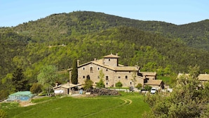 Un edificio de piedra con tejado de baldosas, rodeado de un paisaje verde exuberante y colinas al fondo.