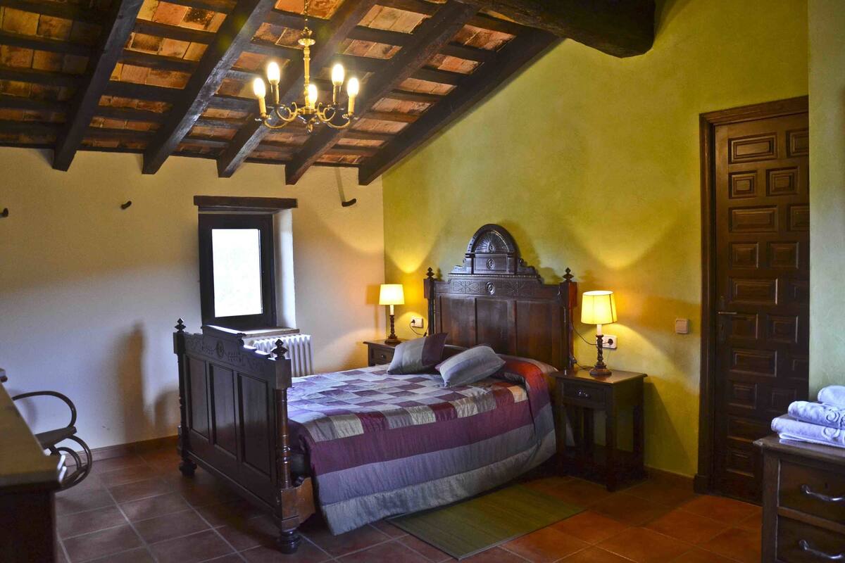 Un dormitorio con una cama de madera, una mesita de noche con lámpara, una ventana y una puerta.