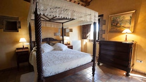 Una cama con dosel y cortina de encaje, un aparador de madera, un cuadro en la pared y dos lámparas de noche.