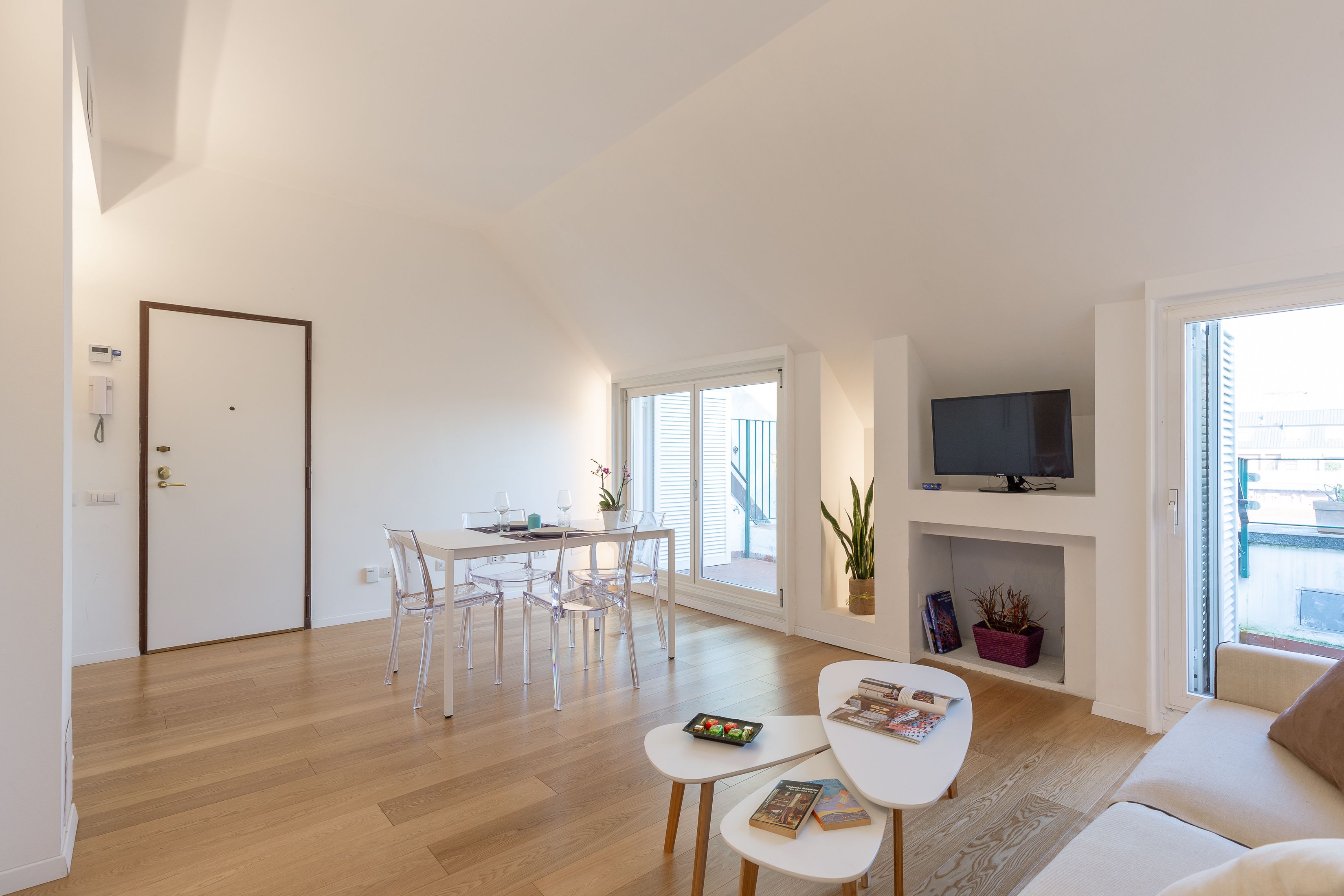 A modern living room with a dining area, a flat-screen TV, and a large window.