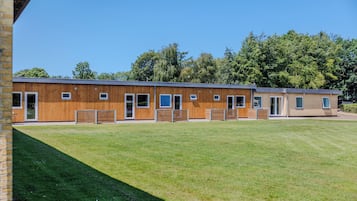 A modern building with a flat roof, multiple windows, and a grassy area in front.