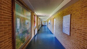 A long hallway with brick walls, blue flooring, and various framed pictures and maps on the walls. - Tønder Byferie (Tonder)
