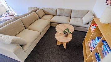 Een modulaire bank, een ronde houten salontafel met een plant en een boekenplank vol boeken.