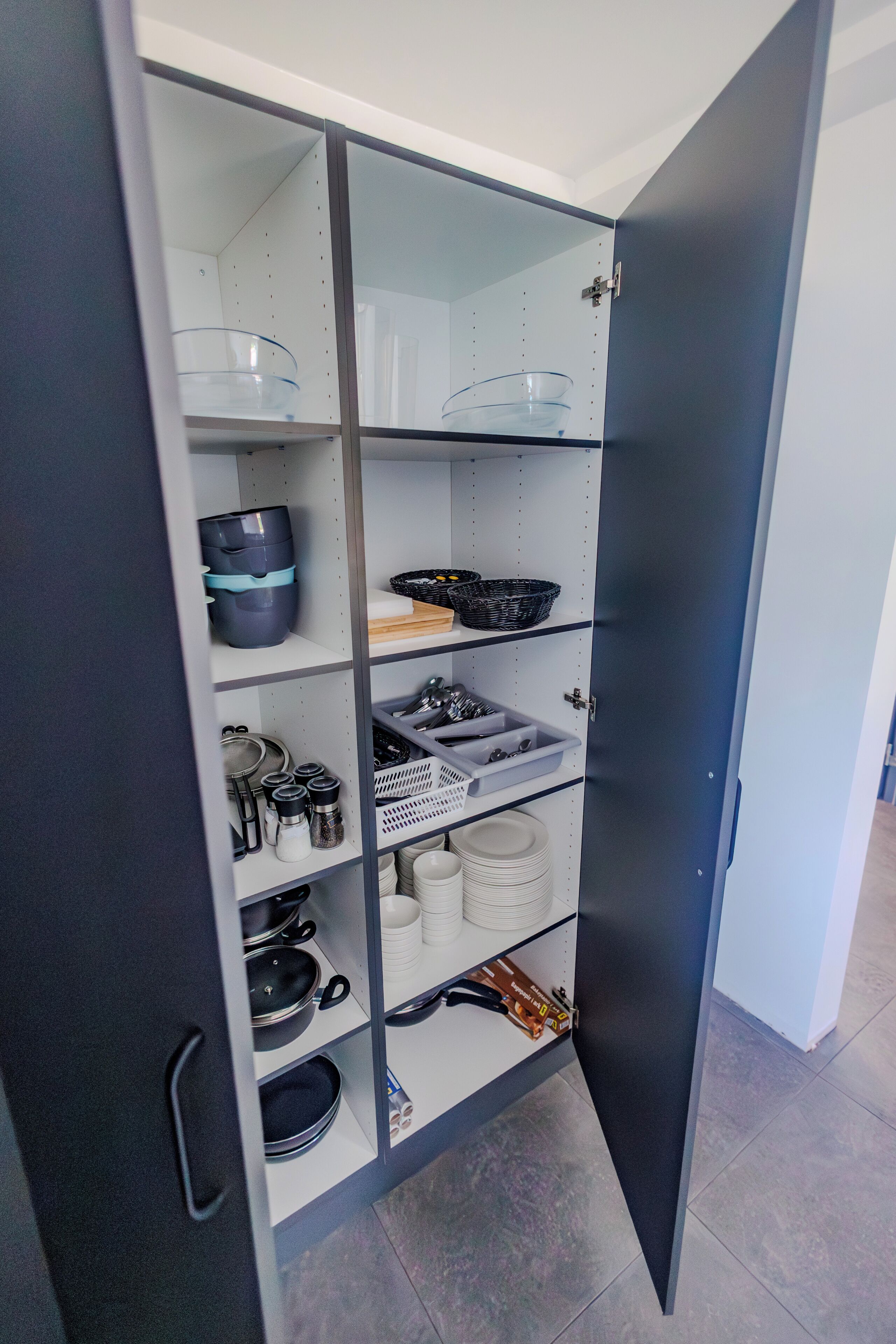 A kitchen with open cabinets, shelves with dishes, and utensils.