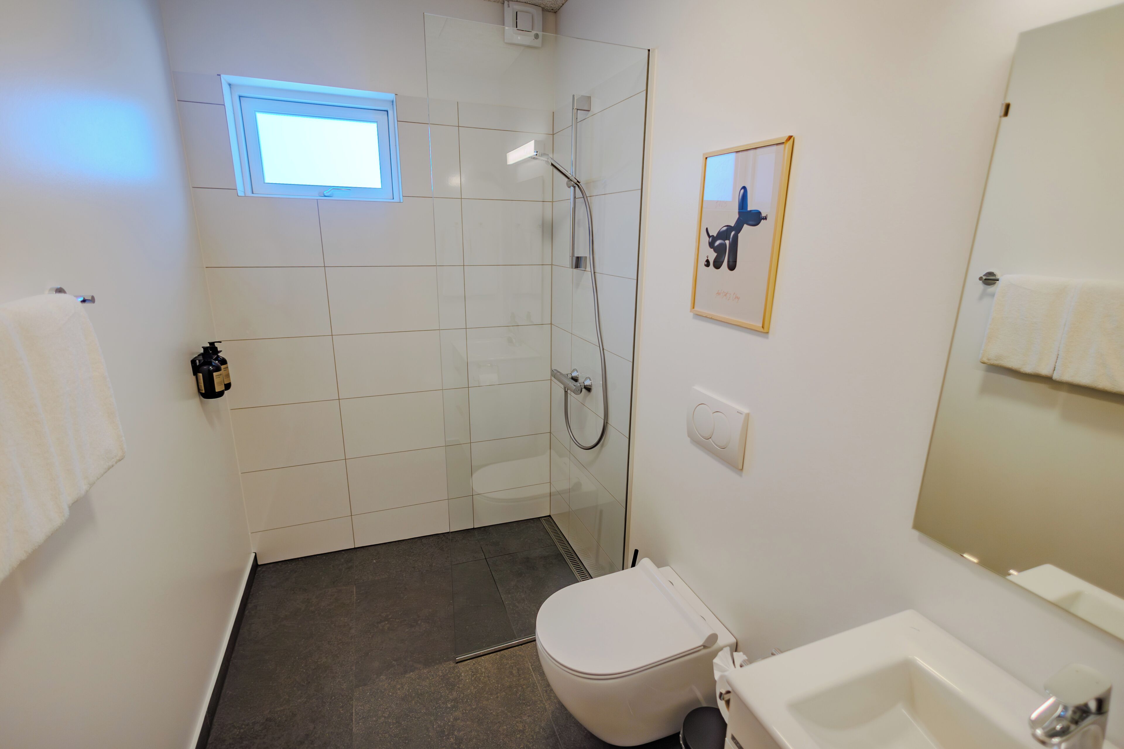 Een badkamer met douche, toilet, wastafel en een klein raam.