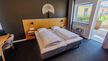 Ein Hotelzimmer mit Bett, Nachttischen, einem Sessel, einem Fenster mit Blick und einem Wandventilator.