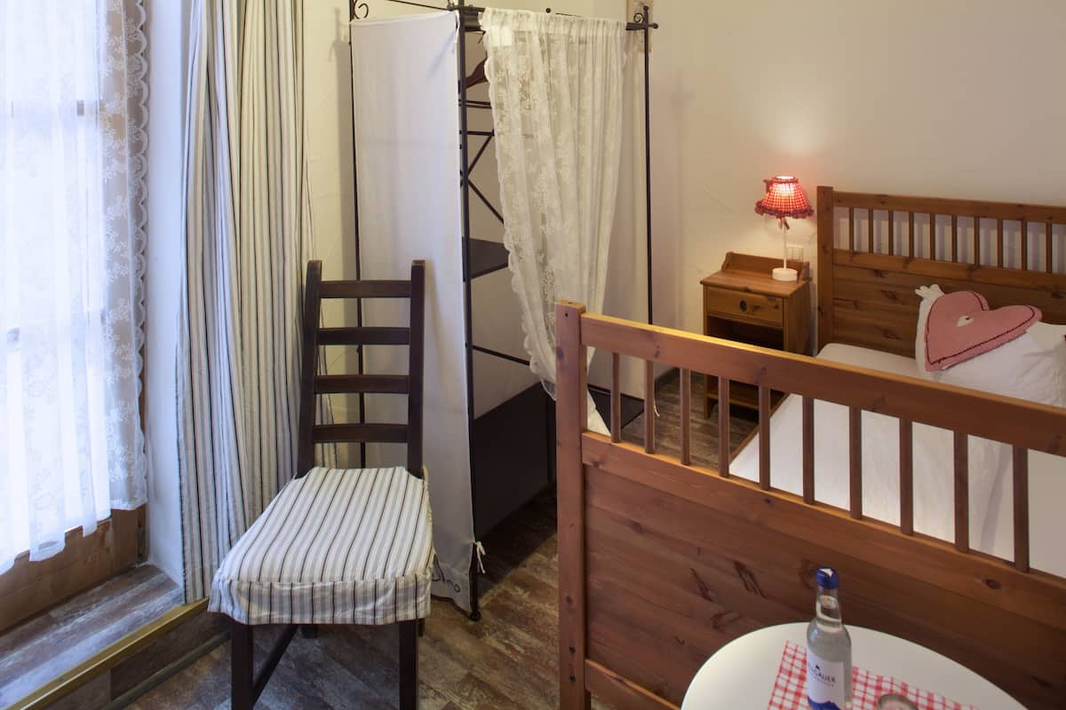 Ein Schlafzimmer mit einem hölzernen Bett, einem Nachttisch mit Lampe, einem Sessel und einem Fenster mit Vorhängen.
