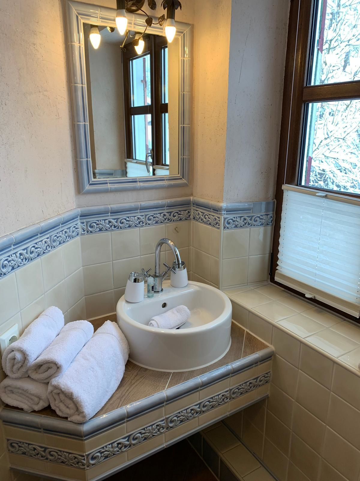 Un baño con lavamanos blanco, un espejo y una ventana con persianas.