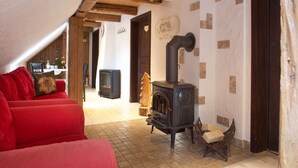 A cozy living room with a red sofa, a wooden chair, a fireplace, and a dining area in the background.