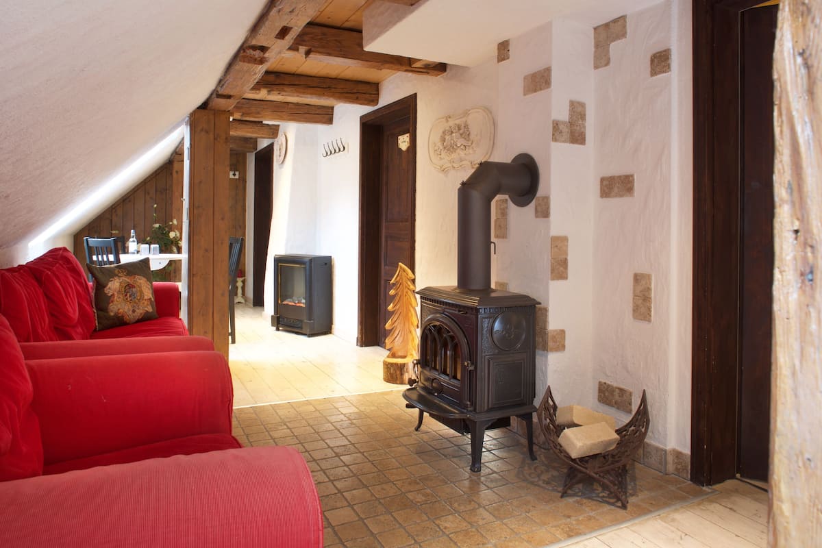 Ein gemütliches Wohnzimmer mit einem roten Sofa, einem Holzstuhl, einem Kamin und einem Essbereich im Hintergrund.