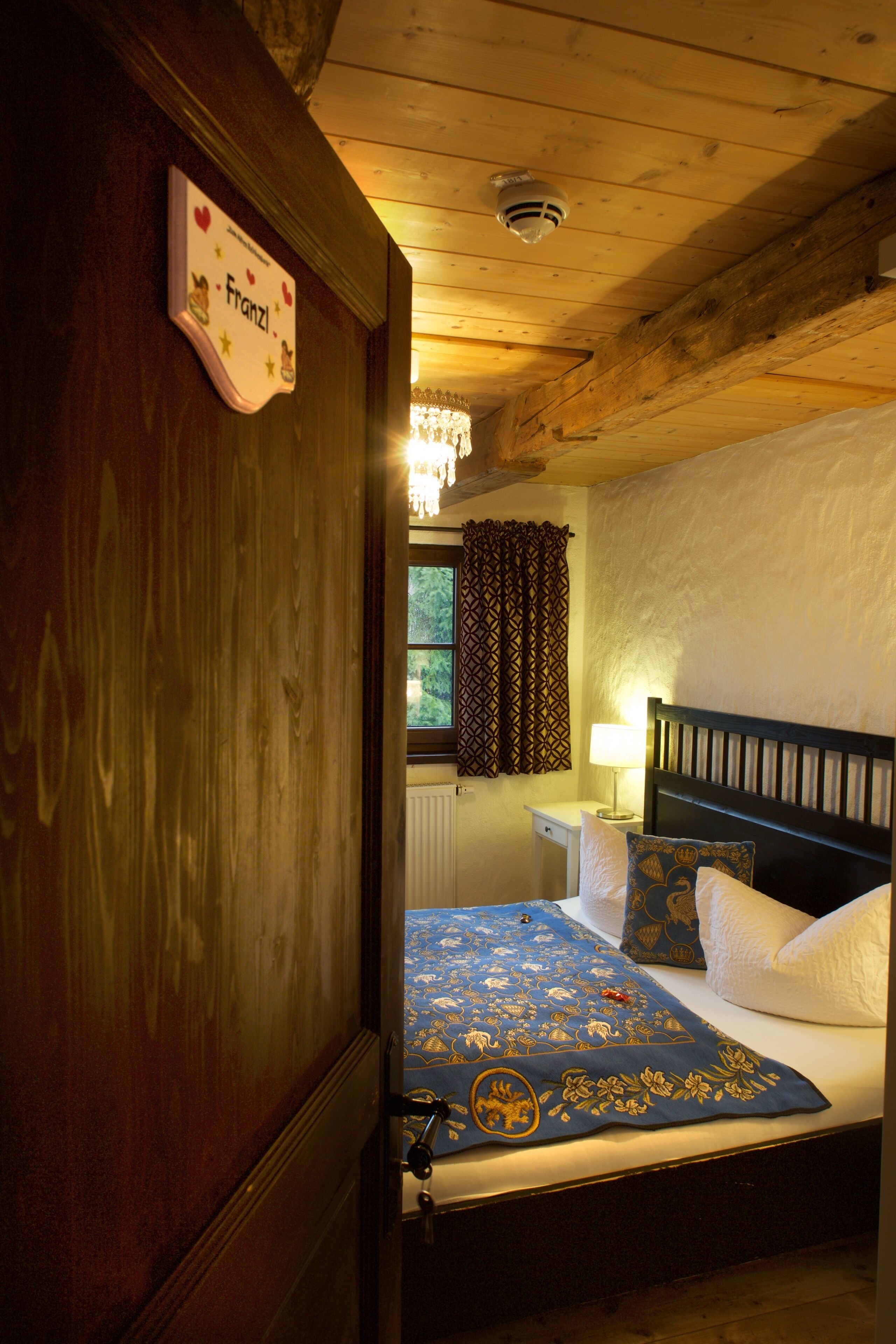 A wooden-framed bedroom with a bed, a nightstand, and a window with curtains.