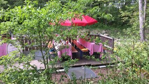 A deck with picnic tables and a red umbrella, surrounded by dense greenery.