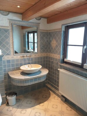 A bathroom with a large mirror, a sink with a basin, patterned tiles, a radiator, and a window with a door.