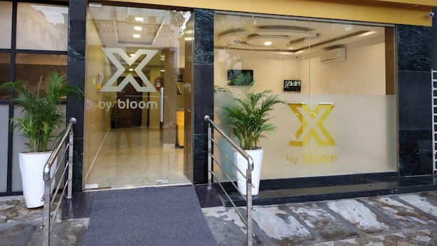 Entrada de un hotel con fachada de vidrio, escalera de metal y plantas en macetas.