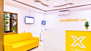 Un área de recepción con un sofá amarillo brillante, un mostrador de recepción blanco y un monitor de ordenador montado en la pared.