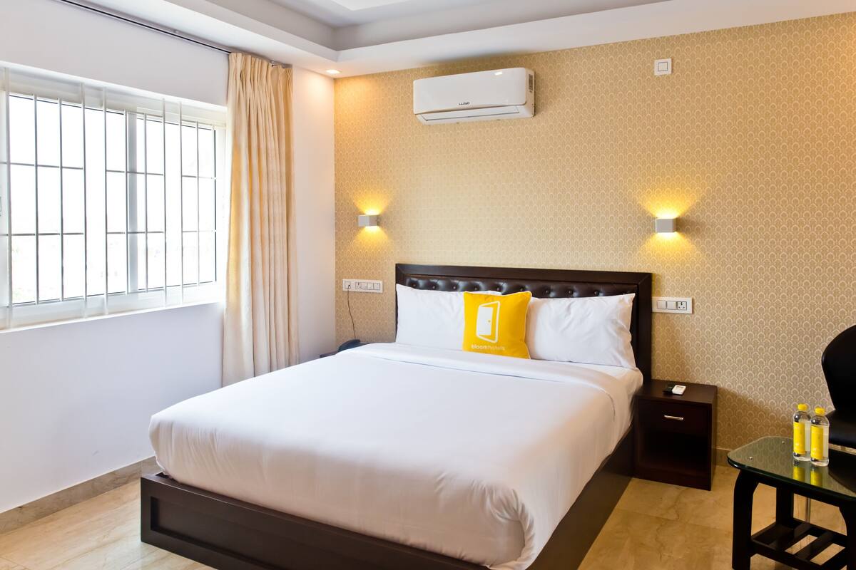 Habitación de hotel con una cama grande, dos mesitas de noche, un equipo de aire acondicionado y una ventana con cortinas.