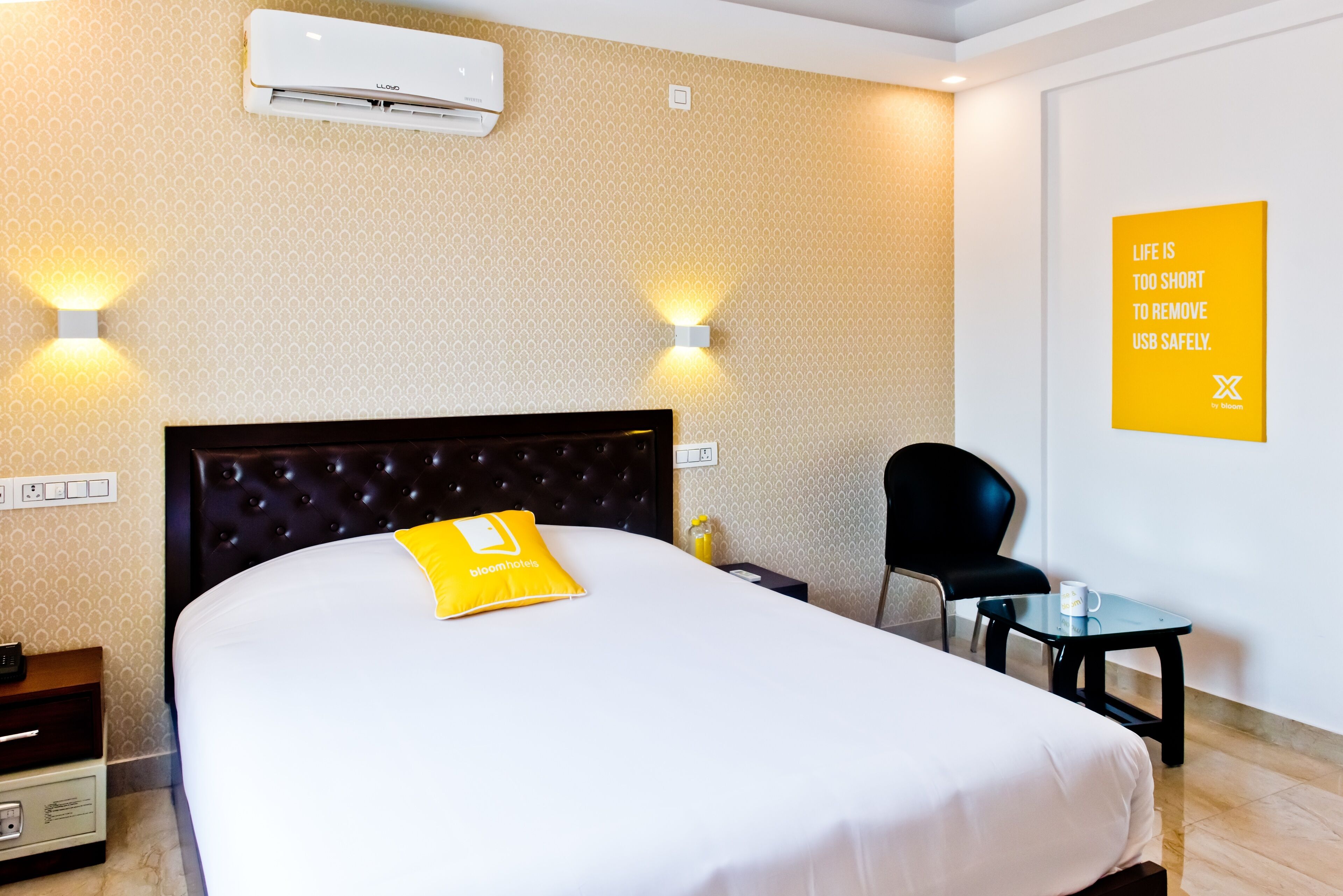 A hotel room with a large bed, a bedside table, a chair, and a small table with a cup.