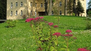 Ein großes, gelbes Gebäude mit vielen Fenstern und einem gepflegten Rasen mit rosa Blumen im Vordergrund.