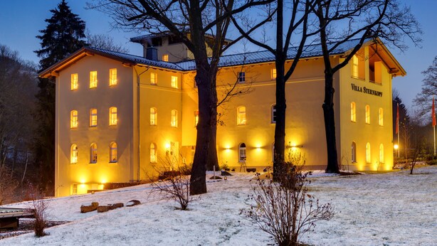 Ein großes, gelbes Gebäude mit vielen Fenstern und einem Schild mit der Aufschrift 'Villa Sternkopf' am Eingang.