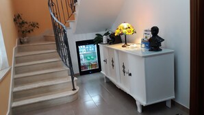 A staircase with a metal railing leading to a landing. A white cabinet with decorative handles is on the landing, and a small table with a lamp and a statue is next to it. A refrigerator with a glass door is visible in the background. - Agriturismo Persichitti (Torricella Peligna)