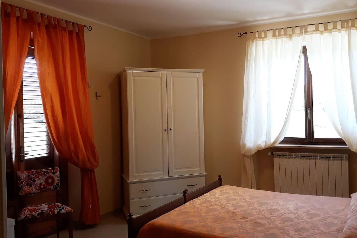 A bedroom with a bed, a wardrobe, a chair, and a window with curtains.