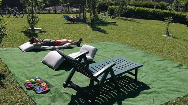 A grassy outdoor area with lounge chairs and a table, a person lying on a cushion, and colorful balls on the ground. - Agriturismo Persichitti (Torricella Peligna)