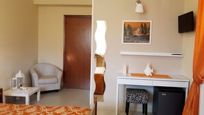 A hotel room with a wooden door, a white desk with a chair, a small table with a decorative item, a wall-mounted TV, and a painting above the desk. - Agriturismo Persichitti (Torricella Peligna)