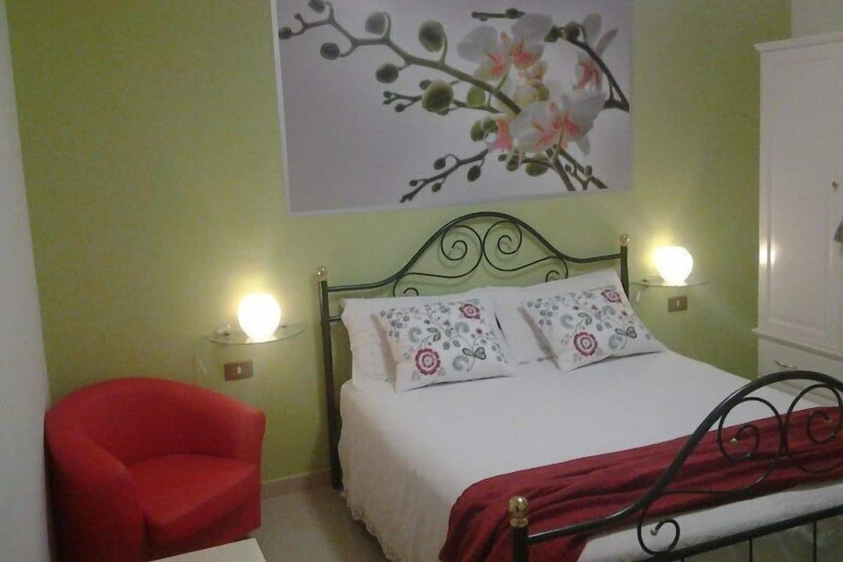 A bedroom with a bed, two bedside lamps, a red chair, and a wall-mounted picture.