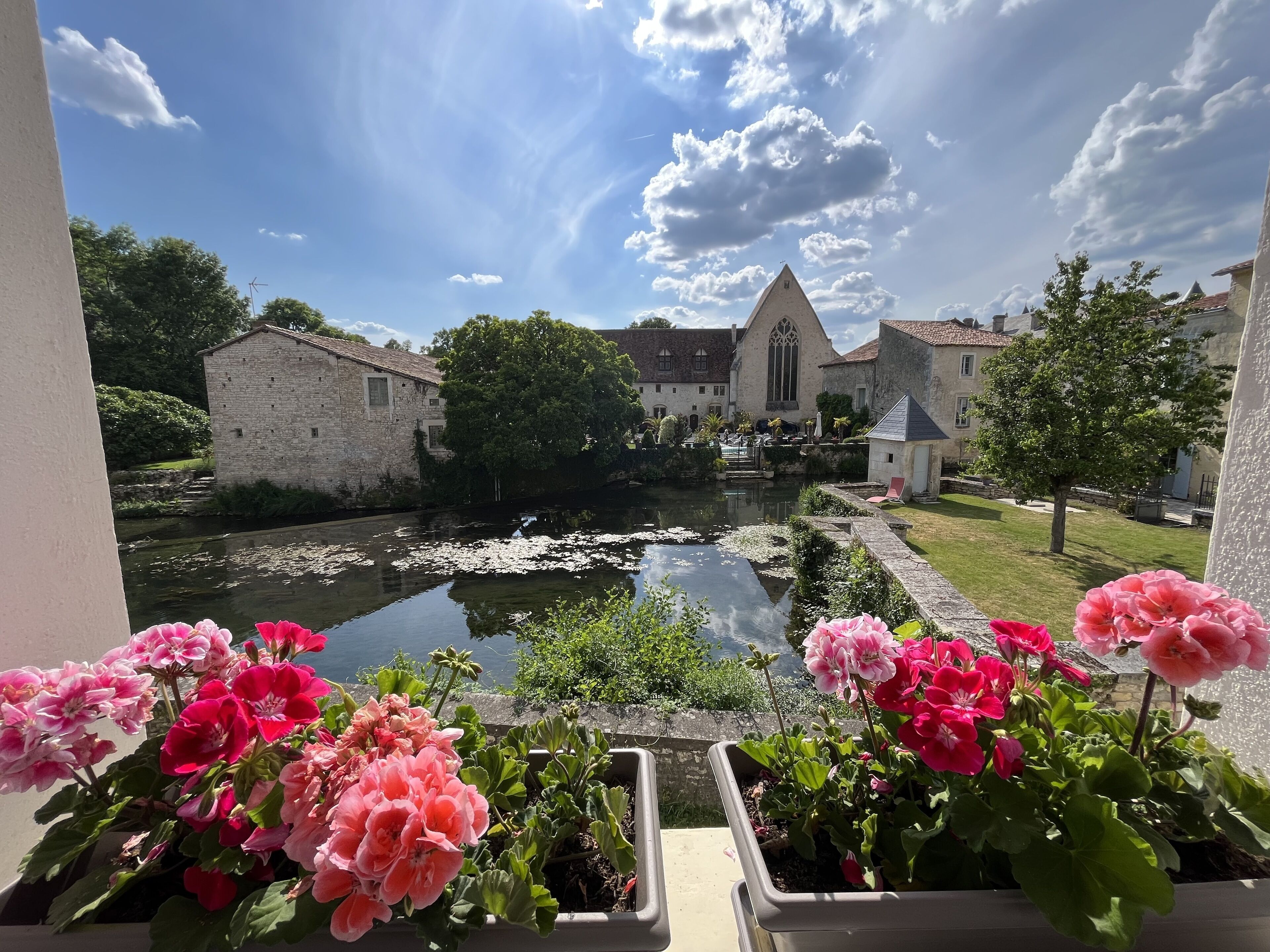 A courtyard with a pond, stone buildings, and flowering plants.