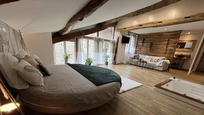A modern bedroom with a large bed, wooden beams, a built-in bathtub, and a cozy seating area. - Les Bruyères (Verteuil-sur-Charente)