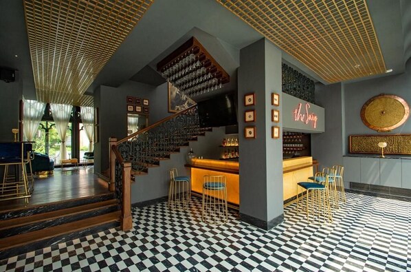 Zona de bar con suelo a cuadros, una escalera y un letrero de neón.