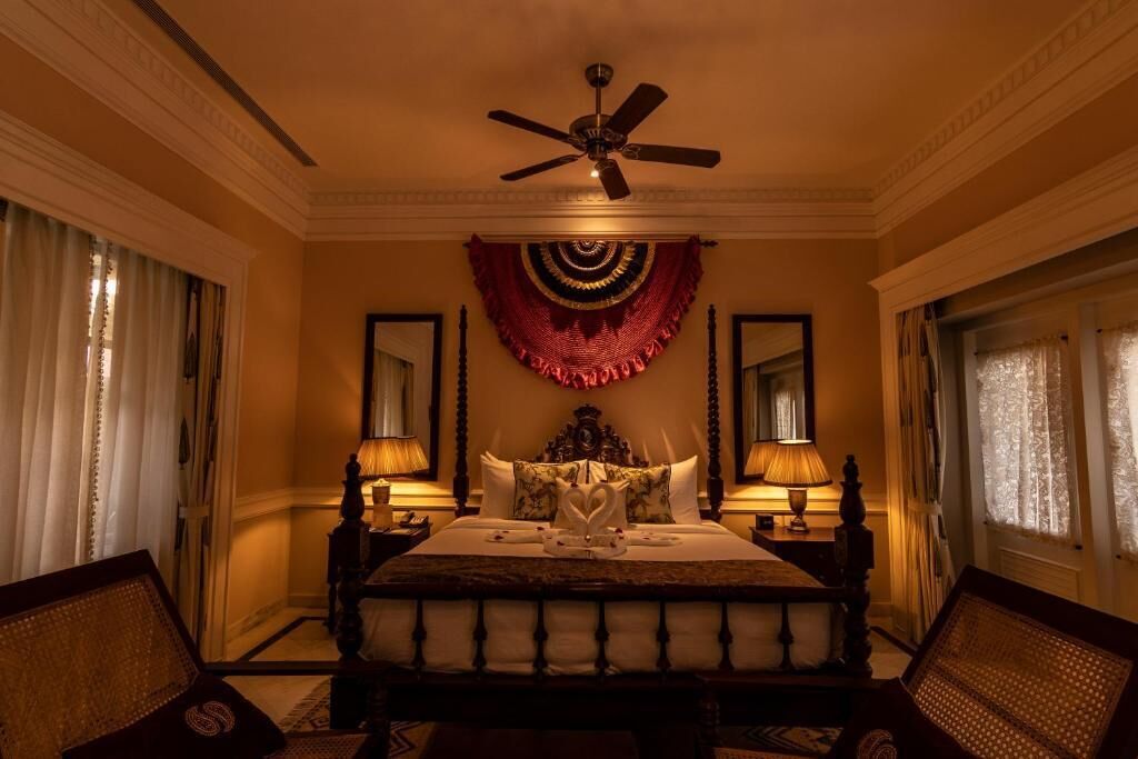 A hotel room with a large bed, two bedside lamps, a ceiling fan, and a decorative wall hanging.