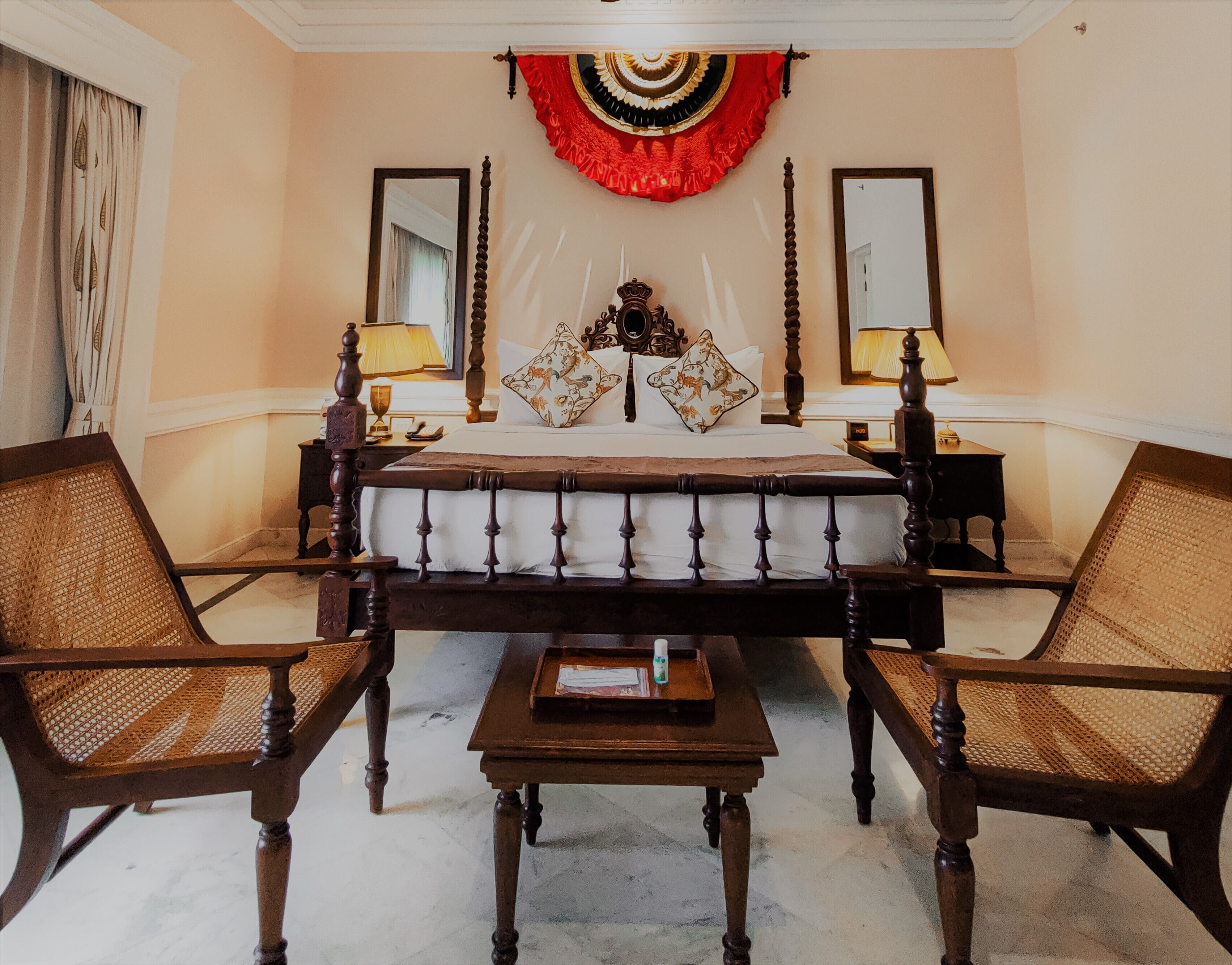 A hotel room with a large bed, two nightstands, two lamps, a mirror, and two wicker chairs.