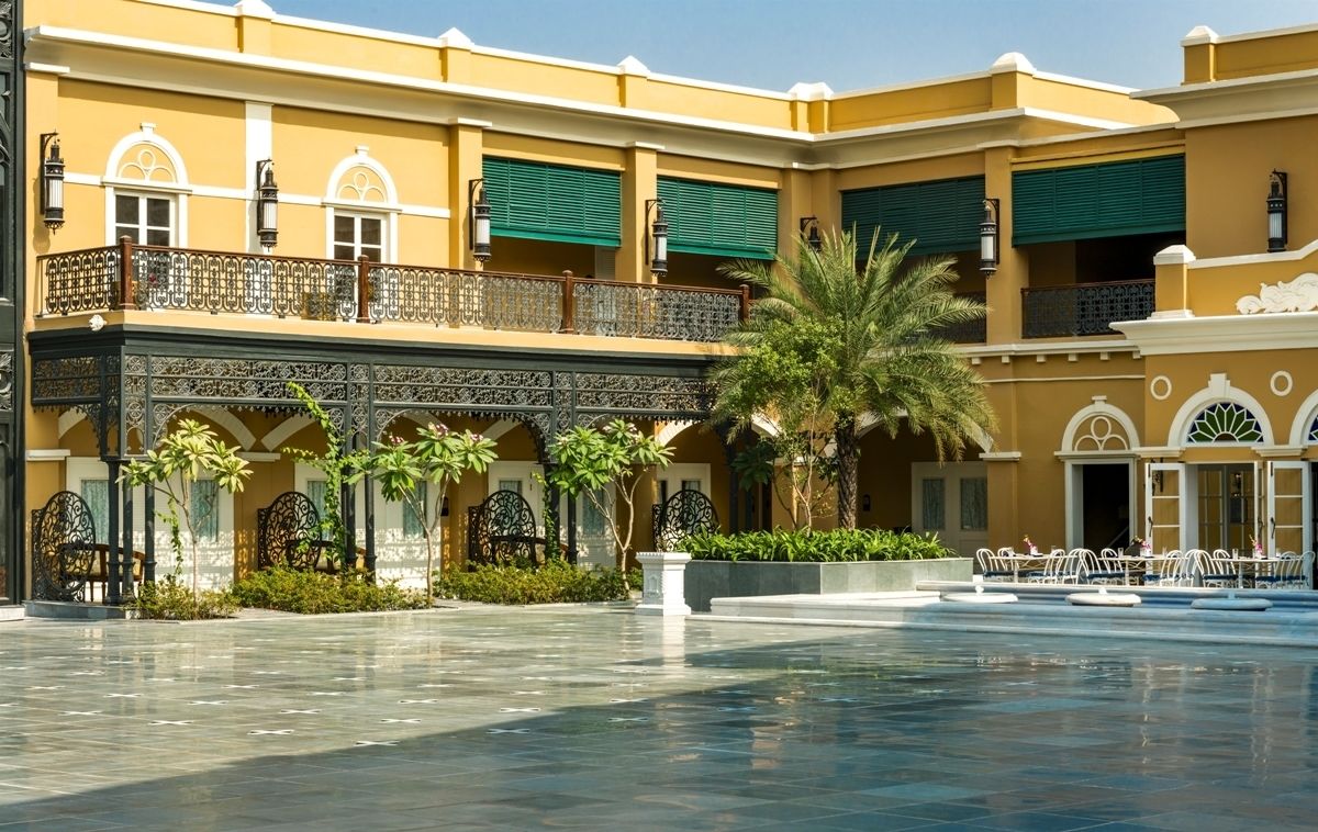 Un patio con piscina, mobiliario exterior y un edificio con balcones y contraventanas verdes.